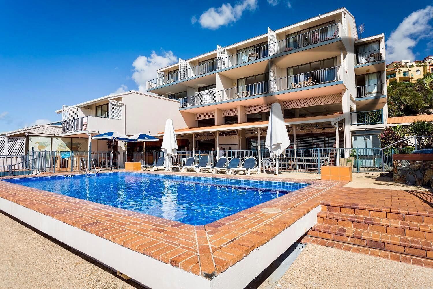 Un hotel con piscina, varios balcones y zonas de estar al aire libre.