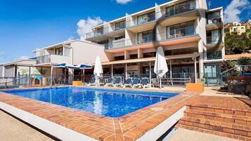 Un hotel con piscina, varios balcones y zonas de estar al aire libre.