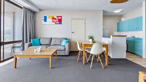Una sala moderna con un sofá gris, una mesa de centro de madera y un comedor con una mesa y sillas blancas.