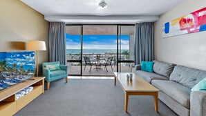 Una habitación de hotel moderna con balcón, sofá, televisor y una mesa.