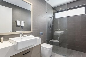 Un baño moderno con un espejo grande, un lavamanos blanco, un inodoro y una zona de ducha con mampara de vidrio.