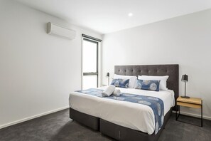 A modern bedroom with a large bed, a nightstand, a lamp, and a window.