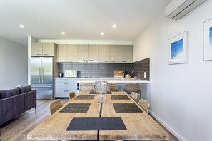 Una cocina moderna con una isla central, un comedor con mesa y sillas de madera, y un sofá gris en la sala de estar.
