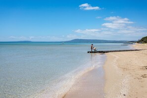 Una playa con aguas cristalinas, un muelle y una montaña distante.