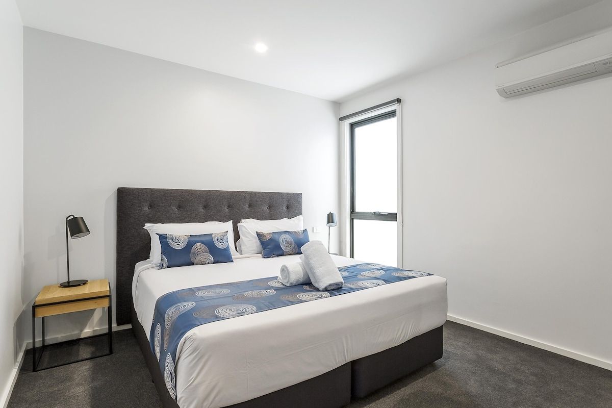 A modern bedroom with a large bed, a bedside table, a lamp, and a window.