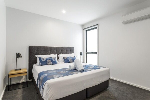Un dormitorio moderno con una cama grande, una mesita de noche, una lámpara y una ventana.