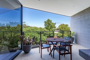 Un balcón con mesa y sillas, una planta en maceta y vistas al verdor.
