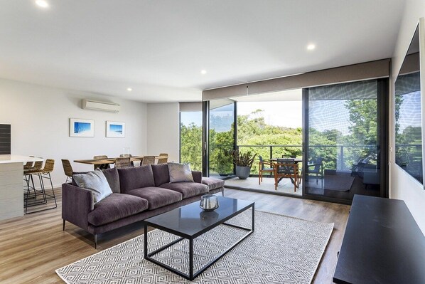 Una sala de estar moderna con un sofá, una mesa de centro y vistas a un balcón con mobiliario exterior.