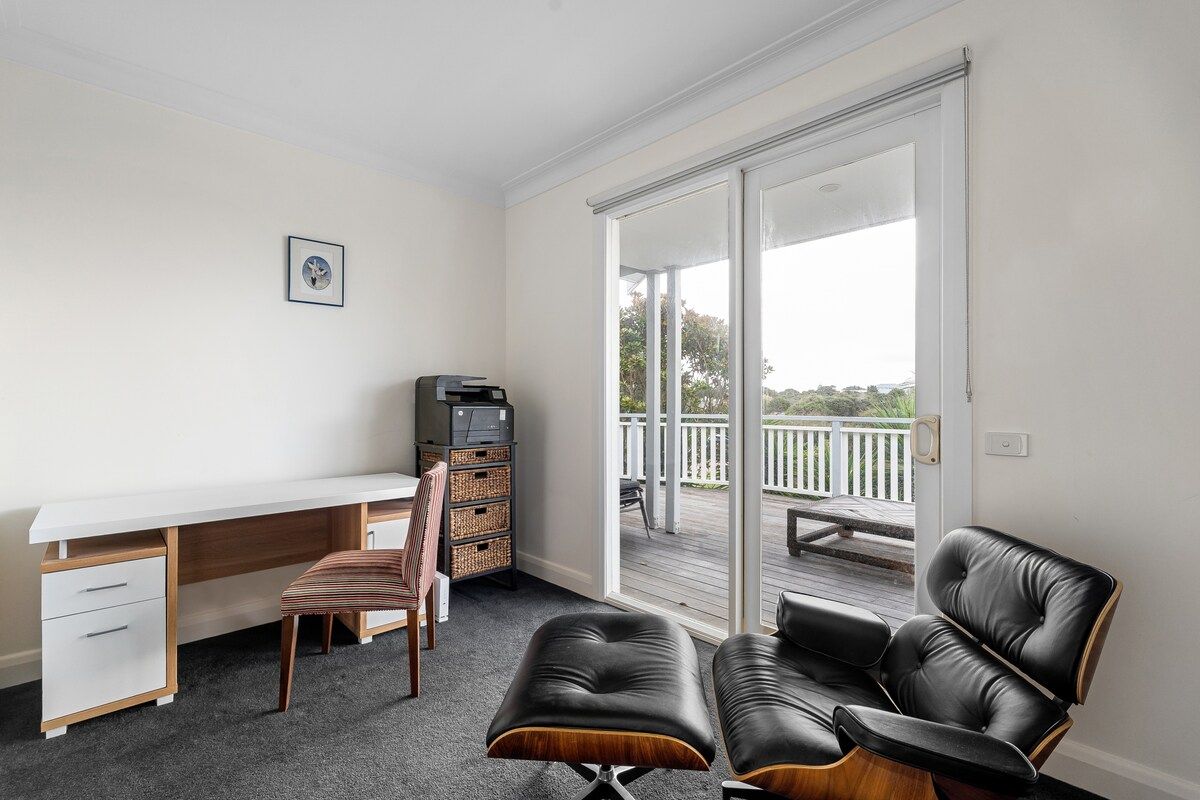 A room with a desk, chair, ottoman, and a sliding glass door leading to an outdoor deck.