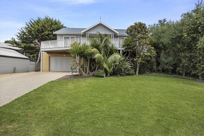 A two-story house with a balcony, surrounded by a well-maintained lawn and various plants.