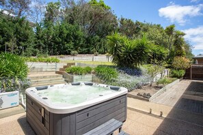 A hot tub in a landscaped garden with steps leading to a wooden deck.
