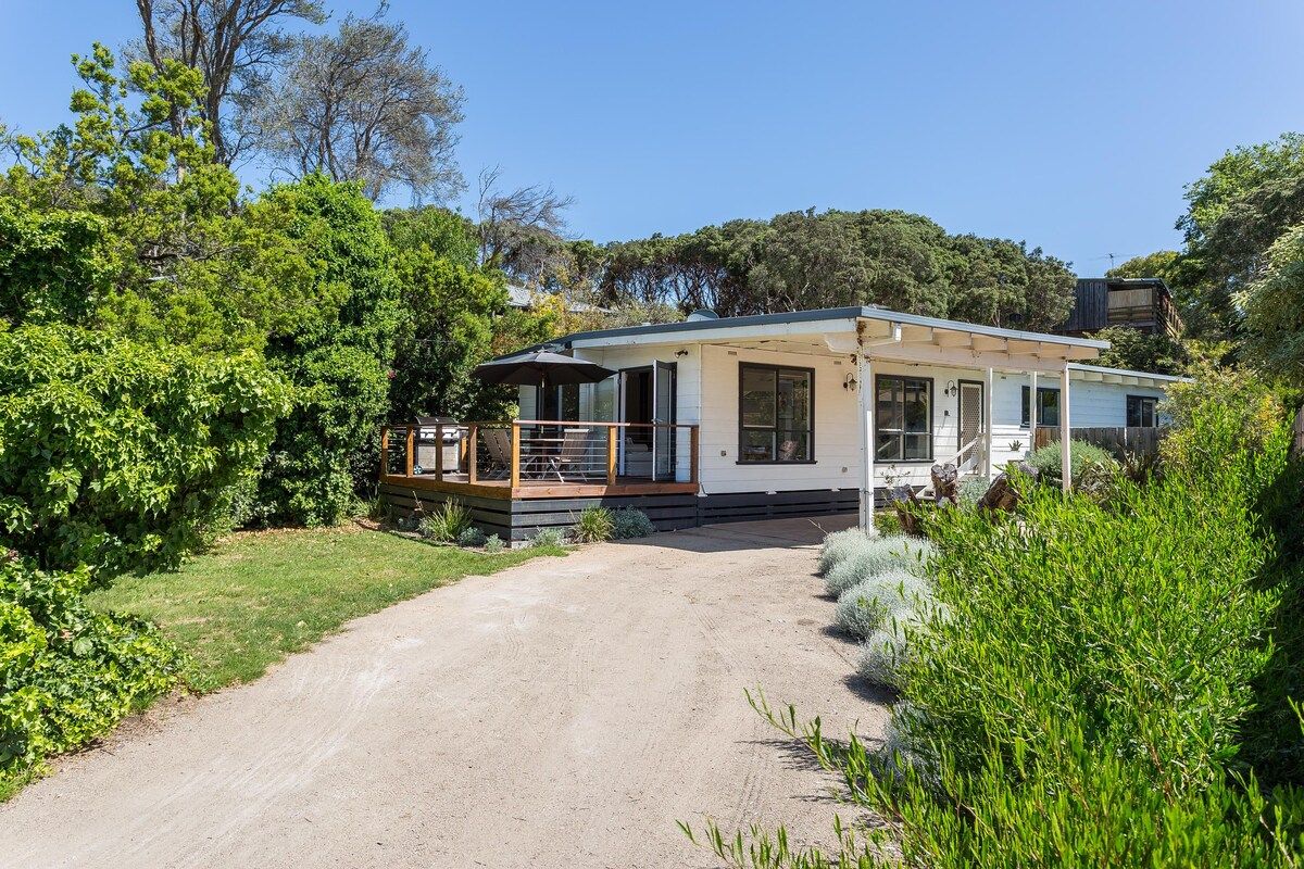 Uma casa térrea com varanda coberta, área de deck aparente e entrada por um caminho de pedras.