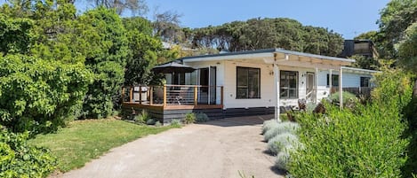 Une maison de plain-pied dotée d’un porche couvert, d’une terrasse bien visible et d’une allée gravillonnée.
