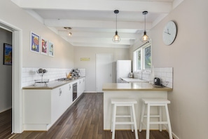 Una cucina moderna con mobili bianchi, un'isola centrale con sgabelli, illuminazione a sospensione e un'ampia finestra.