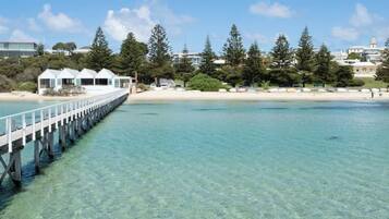 A coastal scene with a pier extending into clear blue water, surrounded by trees and buildings.