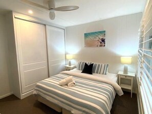 Quarto de hotel com cama, mesas de cabeceira, ventilador de teto, um quadro e uma porta de correr.