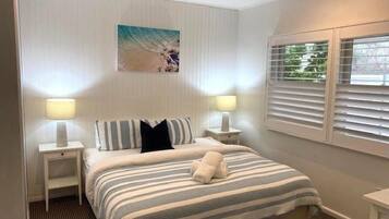 A hotel room with a bed, two bedside lamps, a window with blinds, and a wall-mounted artwork.