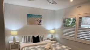 A bedroom with a bed, two bedside tables, a painting on the wall, and a window with blinds.