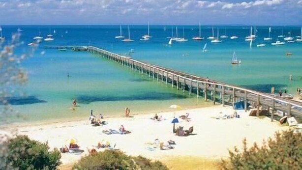 A beach with a pier extending into the sea, surrounded by clear waters and boats.