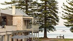 A two-story building with a balcony, outdoor seating with umbrellas, and a view of the sea.