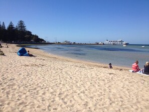 A beach with a sandy shore, a few people, and a large ship in the distance. - Sorrento Beach Cottages #2. (SORRENTO)