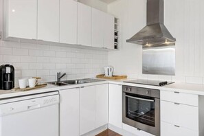 Cozinha moderna com armários brancos, coifa de aço inoxidável, lava-louças e forno.