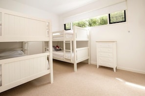 A room with bunk beds, a dresser, and a window with a view of greenery.