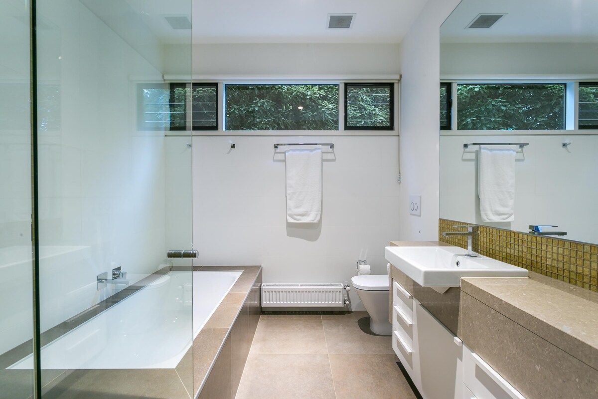 A modern bathroom with a glass shower enclosure, a bathtub, a toilet, and a sink with a mirror above.