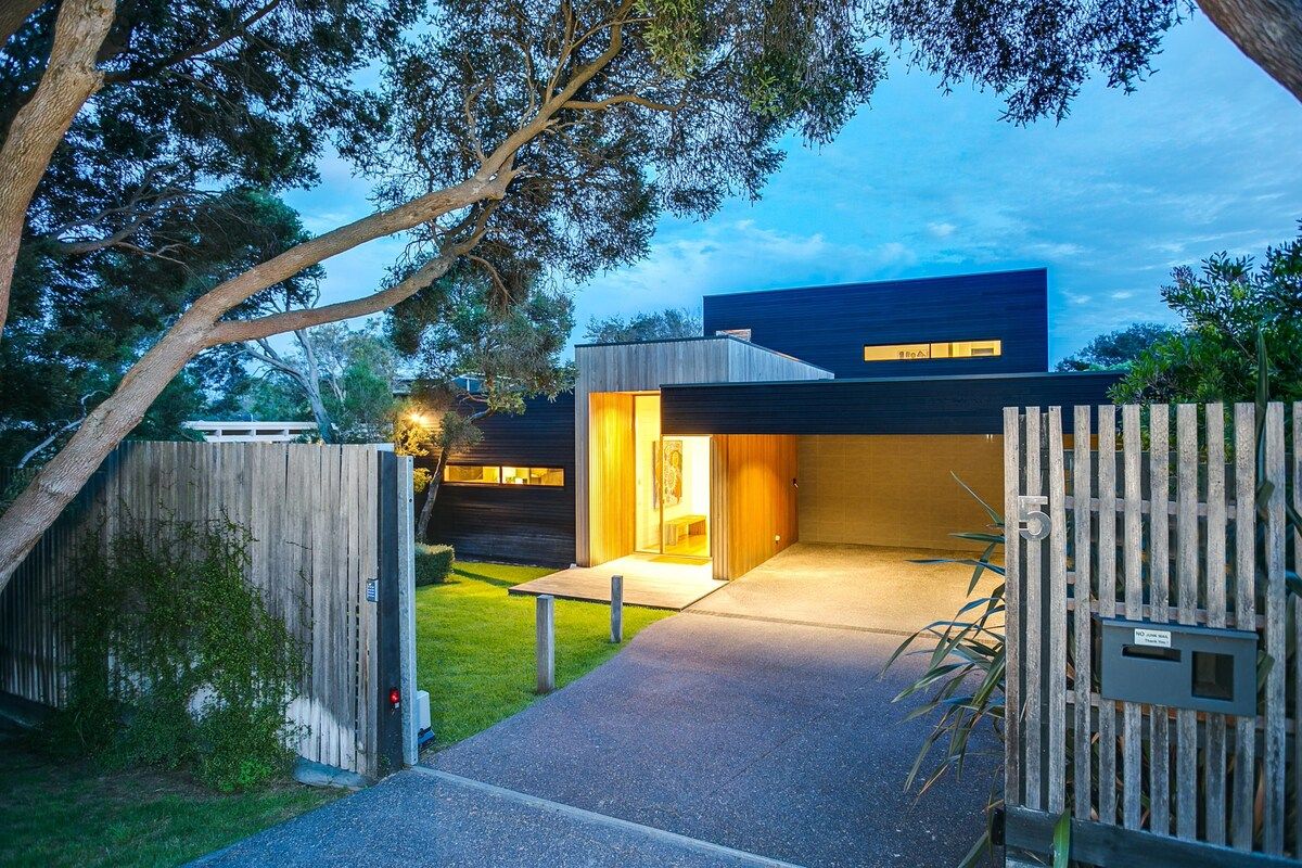 A modern house with a wooden fence, a paved driveway, and a well-maintained lawn.