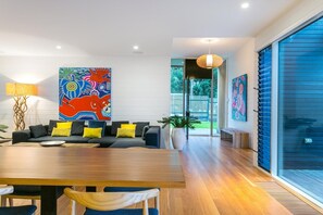 Een modern interieur met een eethoek, een bank met kussens, een groot abstract schilderij en uitzicht door een glazen deur.
