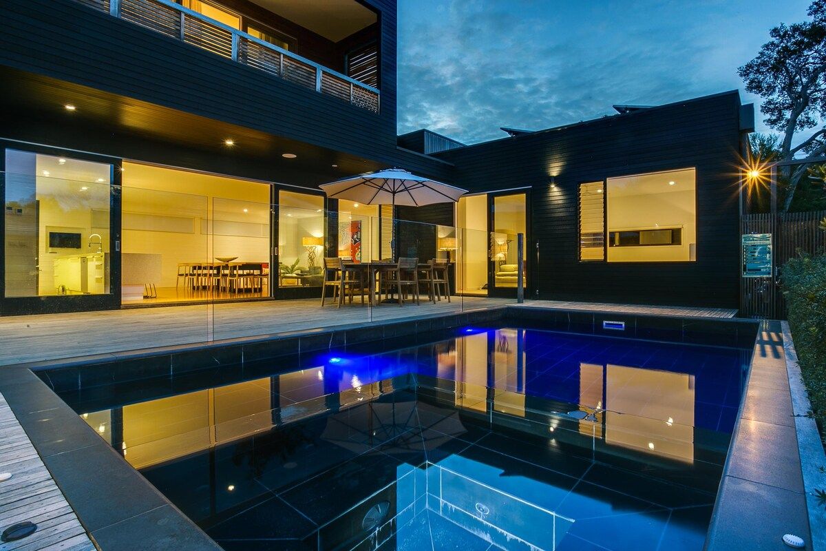 Una casa moderna con piscina, puertas de vidrio y un área de patio.