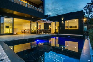 Een modern huis met een zwembad, glazen deuren en een terras.