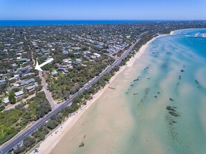 An aerial view of a coastal area with a beach, a road, and a bridge.