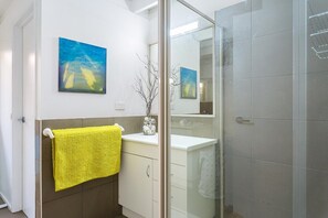 A bathroom with a yellow towel, a glass shower enclosure, and two paintings on the wall. - Sandy's at Rye - renovated. (RYE)