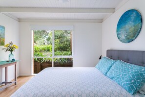 A bedroom with a large bed, a window with a view of greenery, a painting on the wall, and a table with a vase of flowers. - Sandy's at Rye - renovated. (RYE)