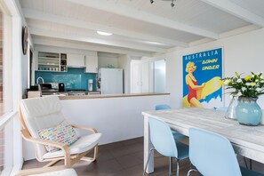 A modern kitchen with white cabinets, a blue backsplash, and a dining area with a wooden table and blue chairs. - Sandy's at Rye - renovated. (RYE)