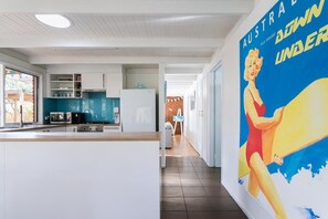 A modern kitchen with white cabinetry, a built-in microwave, and a refrigerator. There is a large poster on the wall depicting a woman surfing. - Sandy's at Rye - renovated. (RYE)