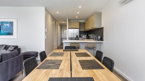 A modern kitchen with a central island, a dining area with a wooden table and chairs, and a living area with sofas and a framed picture.