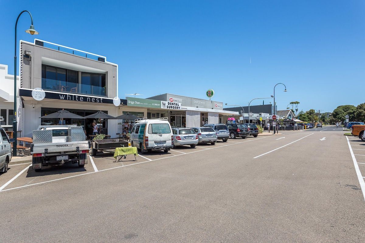 A street view with a row of parked cars, a building with a sign for 'white nest,' and a 'dental surgery' sign.