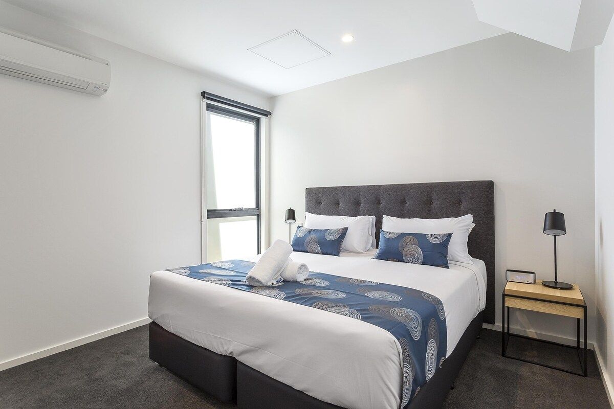 A modern hotel room with a large bed, a bedside table, and a window.