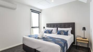 A modern hotel room with a large bed, a bedside table, and a window.