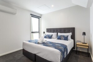 Ein modernes Hotelzimmer mit einem großen Bett, einem Nachttisch und einem Fenster.