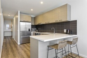 Eine moderne Küche mit einer zentralen Kochinsel, Edelstahlgeräten und einer dunkel gefliesten Spritzschutzwand.