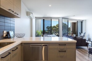 A modern kitchen with a dishwasher, wooden cabinets, and a large window overlooking a dining area.