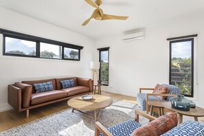 Een moderne woonkamer met een bruine leren bank, decoratieve kussens, een ronde salontafel en een plafondventilator.