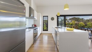 A modern kitchen with stainless steel appliances, a central island, and a view of the outdoors through large windows. - Yaringa, St Andrews Beach - Pristine new family living and only moments from the surf beach (ST ANDREWS BEACH)