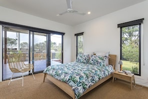 A bedroom with a bed, a chair, a nightstand, and a view of the outdoors.