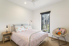 Een slaapkamer met een bed, nachtkastje, lamp, stoel en een raam.