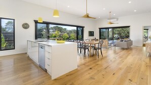 A modern kitchen with a central island, large windows, and a dining area with a sofa and chairs. - Yaringa, St Andrews Beach - Pristine new family living and only moments from the surf beach (ST ANDREWS BEACH)