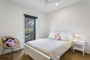 A bedroom with a bed, a chair, a bedside table, and a window.